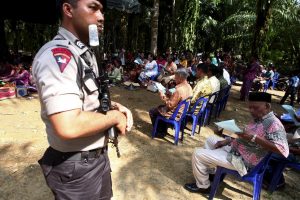 An Indonesian policeman holds a rifle as he guards residents during Sunday mass prayer beside a burned church at Suka Makmur Village in Aceh Singkil